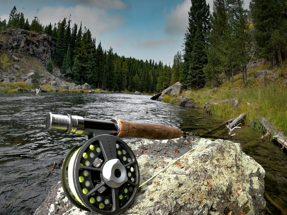 Fly-fishing rod and reel resting on a rock beside a river.