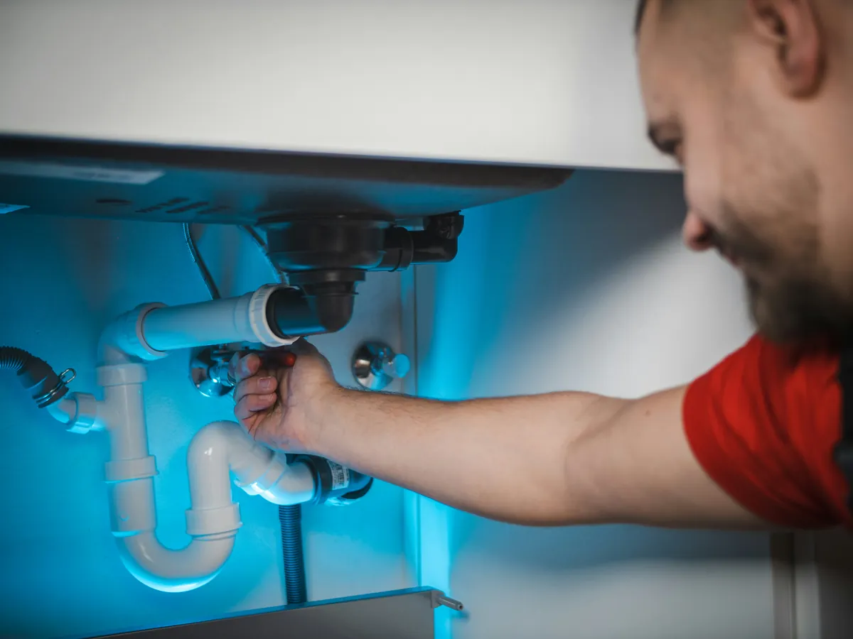 Plumber working on drain pipework beneath a sink.